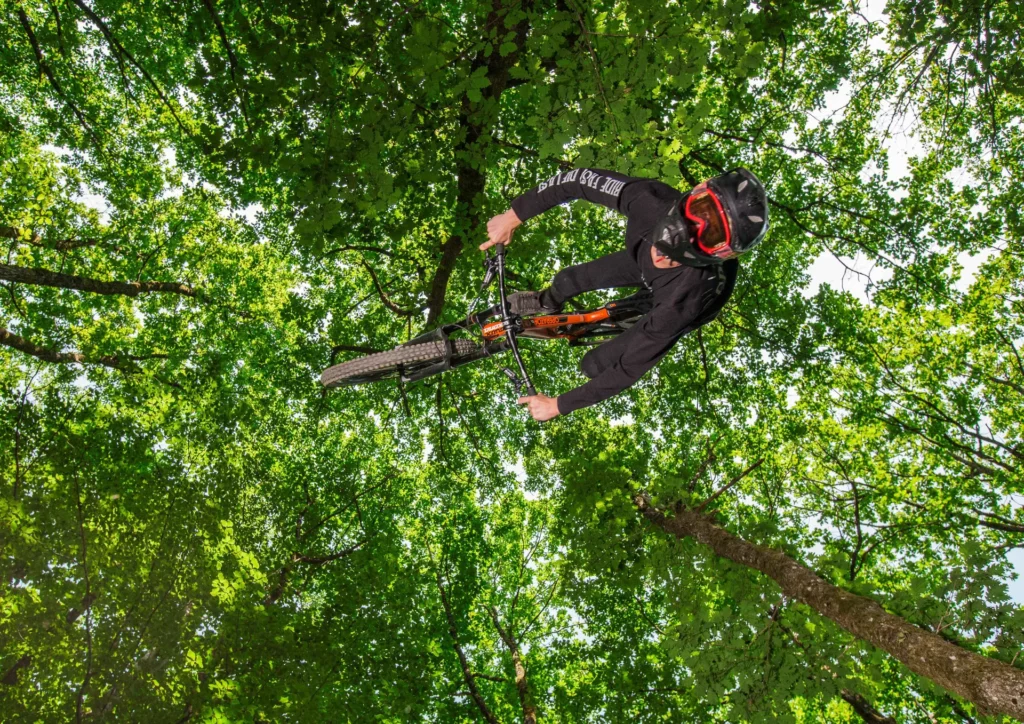 VTT freestyle en pleine nature – Tijoe photographe Mulhouse Rider VTT effectuant une figure aérienne au milieu d'une forêt verdoyante