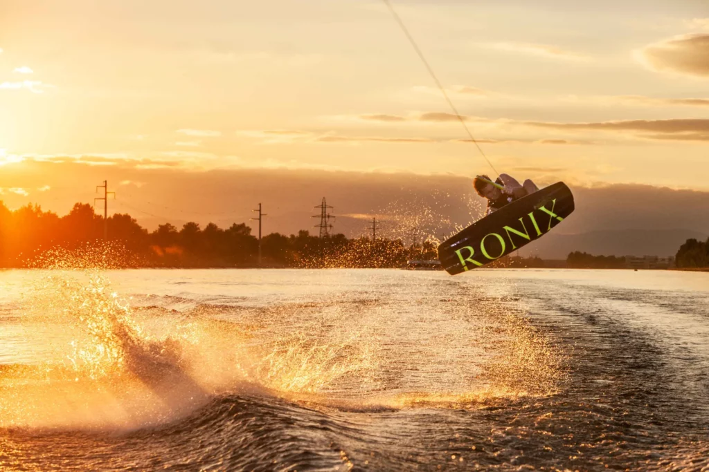 Figure de wakeboard au coucher du soleil – photographie sportive dynamique – Tijoe photographe Wakeboarder effectuant une figure au coucher de soleil avec éclaboussures sur l’eau