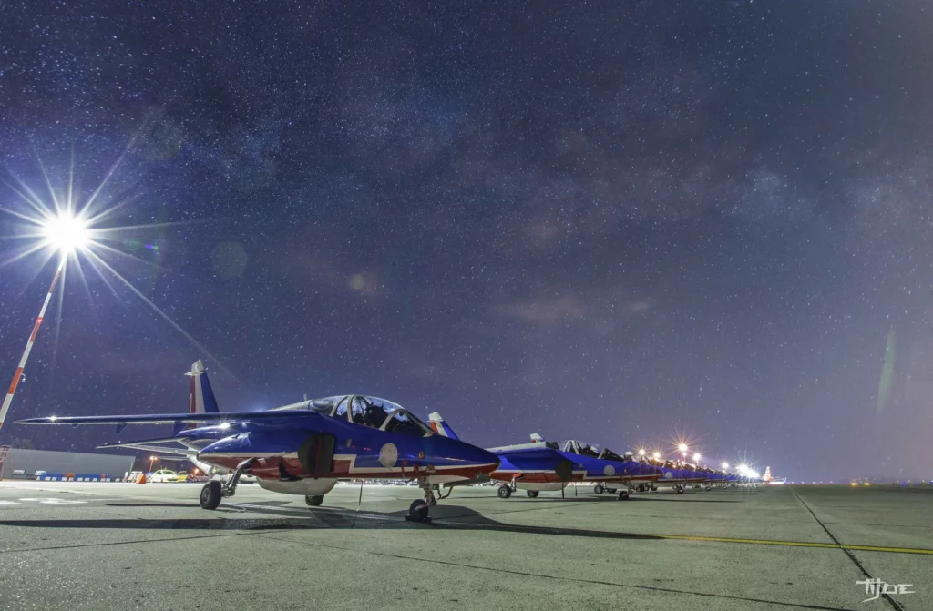 Patrouille de France – Avions sous la Voie lactée, nuit étoilée sur piste aérienne Avions de la Patrouille de France alignés sur le tarmac sous un ciel étoilé avec la Voie lactée
