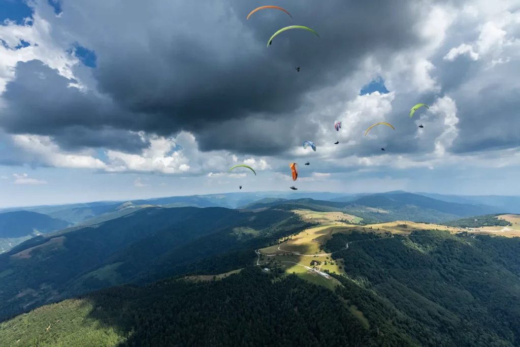 Parapente en montagne – photo signée Tijoe, photographe professionnel à Mulhouse Vol de parapentes au-dessus des montagnes sous un ciel nuageux – photo de Tijoe, photographe à Mulhouse