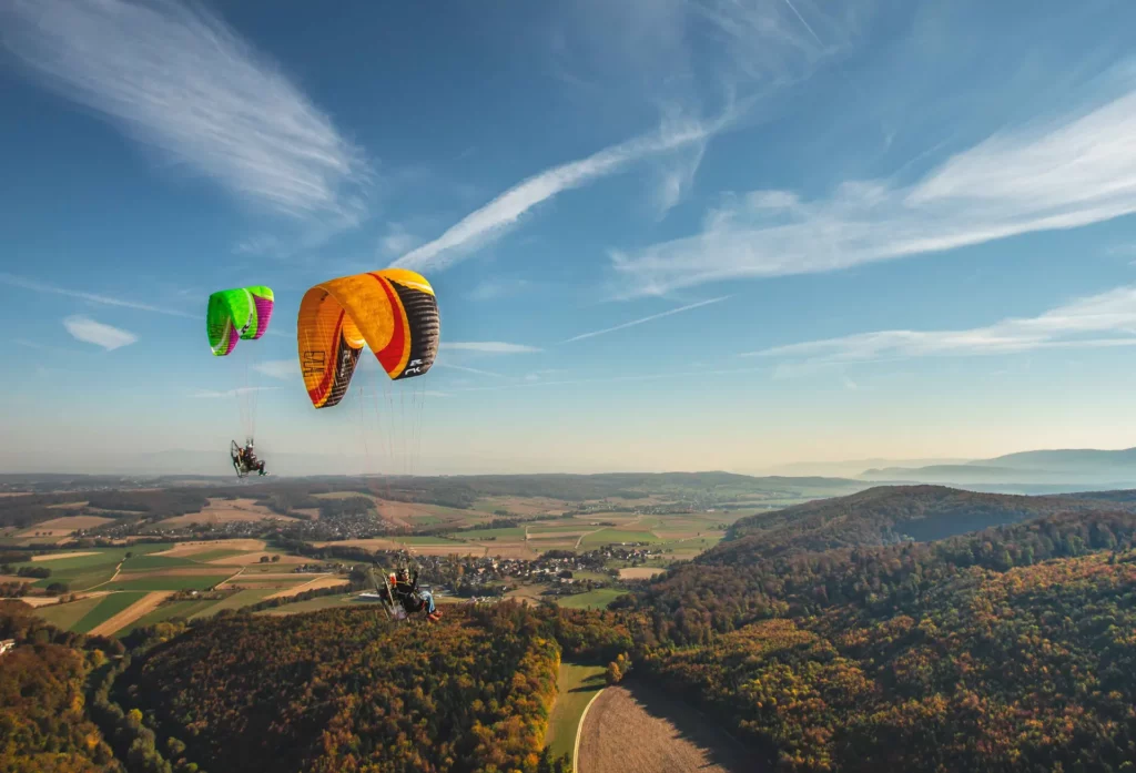 Photo de paramoteur signée Tijoe – sport aérien au-dessus de la campagne alsacienne Paramoteurs en vol au-dessus d’un paysage vallonné – photo de Tijoe, photographe professionnel à Mulhouse