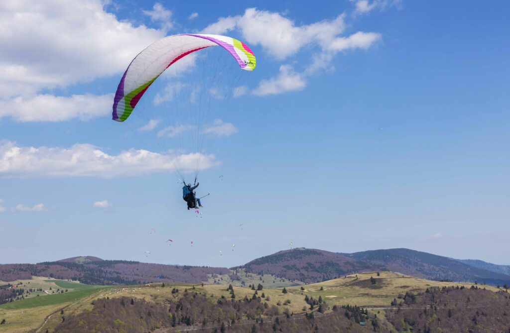 Parapente biplace survolant les montagnes des Vosges par ciel bleu en Alsace, photo par Tijoe