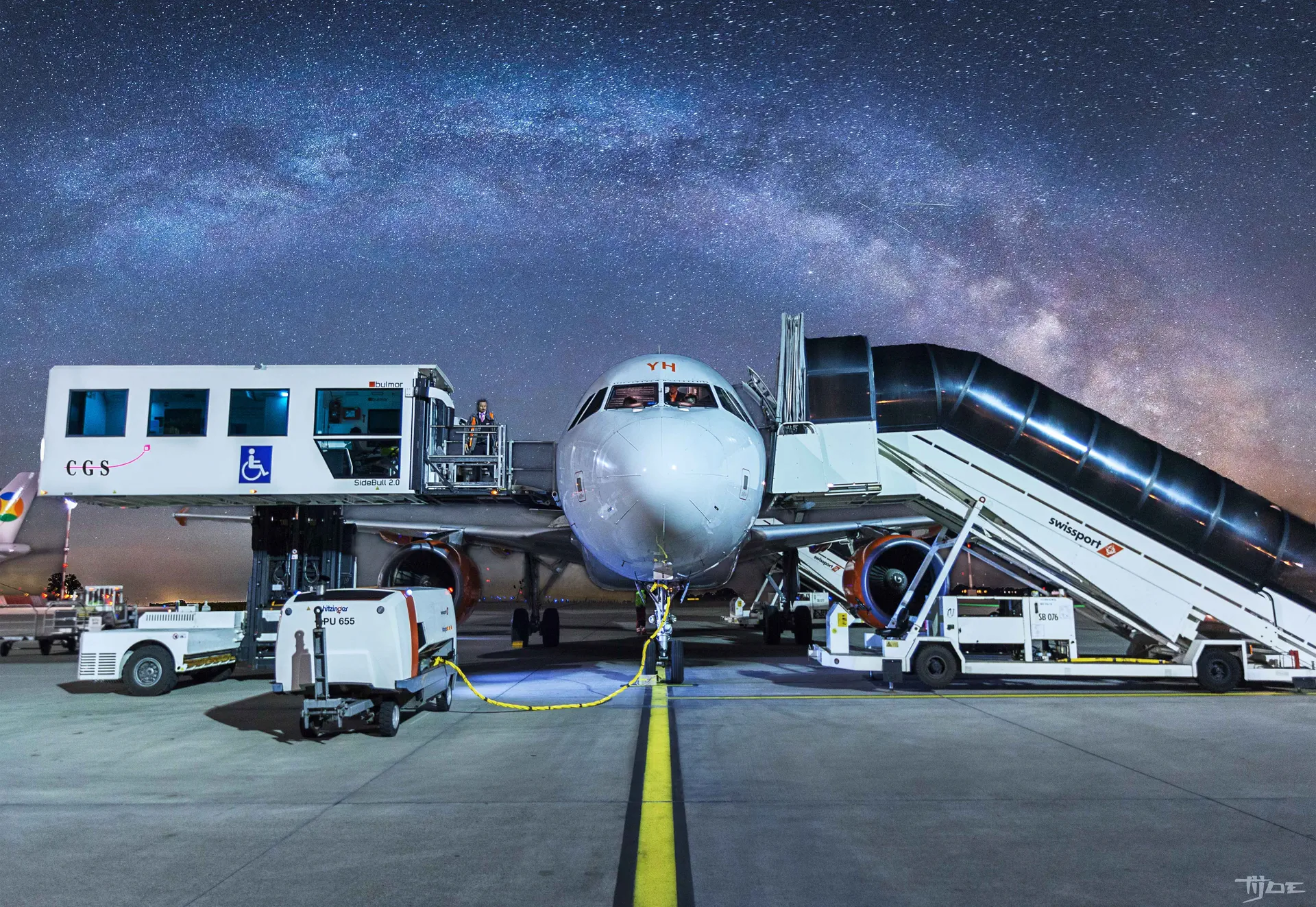 Photographie aéronautique : avion de ligne et passerelle Swissport sous la Voie lactée Avion de ligne au sol la nuit avec passerelle Swissport – photographie professionnelle aéronautique