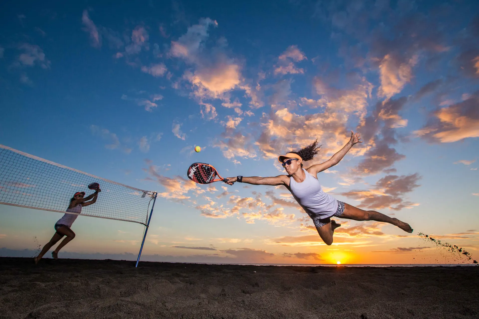 Action intense de beach tennis sur la plage au coucher du soleil Joueuse de beach tennis en plein smash au coucher du soleil