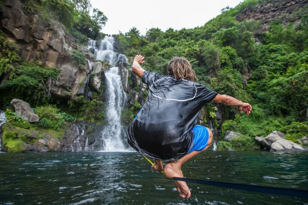 Slackliner traversant une rivière devant une cascade tropicale