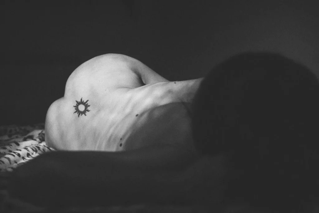 Photographie artistique en noir et blanc d’un dos nu avec un tatouage soleil, en lumière douce