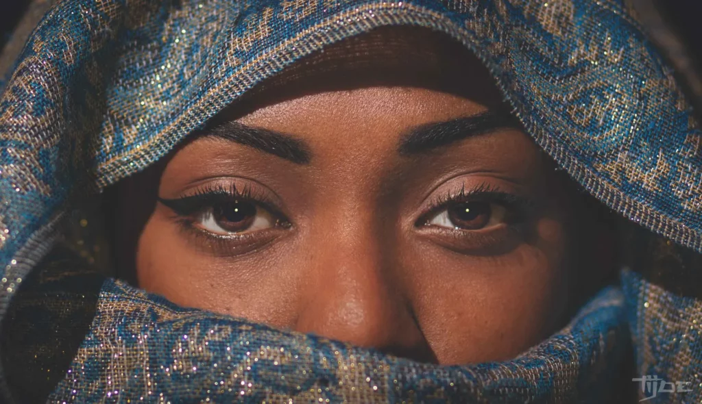 Gros plan sur les yeux d’une femme portant un voile bleu brodé, regard intense et expressif